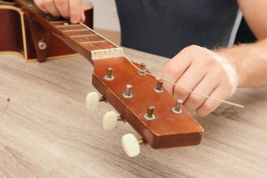 Evde gitarın tellerini değiştiren bir adam. Akustik gitarın telini değiştiren genç bir adamın elleri..