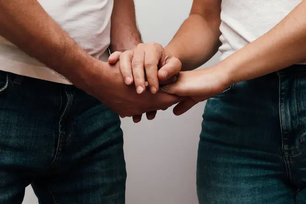 Cropped shot of an unrecognizable couple in jeans wear holding hands, close-up. Close up of caucasian couple holding hands. Love and care concept.