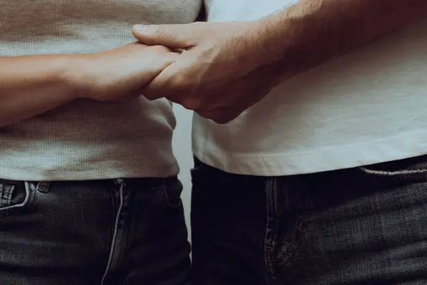 Cropped shot of an unrecognizable couple in jeans wear holding hands, close-up. Close up of caucasian couple holding hands. Love and care concept.