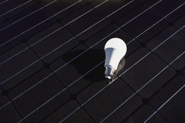 LED lamp bulb on the background of a solar panel. The concept of saving money, clean energy and green renewable energy. Space for text.