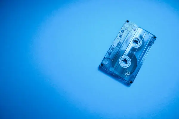 Old vintage transparent audio cassette tape photo on blue background. Place for text.