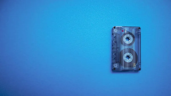 Transparent audio cassette tape photo on blue background. Place for text.
