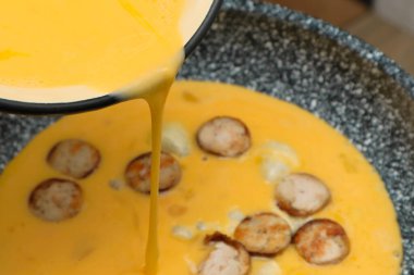 Sosisli omlet yapıyorum. Çırpılmış yumurta için sıvı yumurta kızartma tavasına dökülüyor..