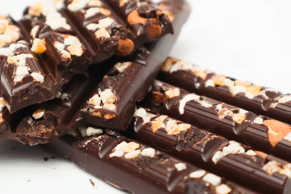 Pieces of broken tasty dark chocolate with hazelnut on white background. Selective focus. Dark Chocolate bar with peanuts pieces.