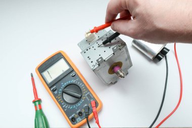 Mikrodalga fırının onarımı. Ustanın elleri, yüksek voltajlı güç kapasitörünü ve magnetronu multimetre ile kontrol ediyor.