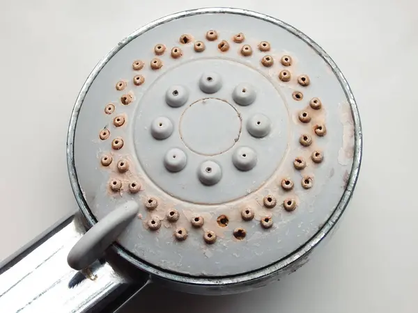 Silver round shower head with hard water deposits, limescales closeup. Calcified shower due to hard water. Selective focus on hard water deposit.