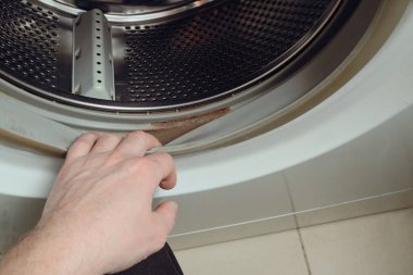 Dirty moldy washing machine sealing rubber. The person checks the dirt on the rubber of a washing machine. Cropped hand holding washing machine. Rubber seal on washing machine drum clipart