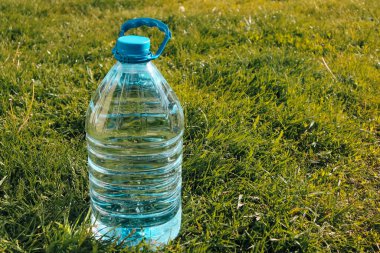 İçme suyu. Yeşil çimen arka planında plastik içme suyu şişesi. Plastik paket ürünü.