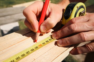 Bir marangoz bir tahta parçasını mezura ve kalemle işaretler. Tahta kalas ölçüsü ve kalemle işaretleme. İnşaatçı, tamirci kalem izi yapıyor..