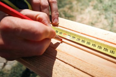 Bir marangoz bir tahta parçasını mezura ve kalemle işaretler. Tahta kalas ölçüsü ve kalemle işaretleme. İnşaatçı, tamirci kalem izi yapıyor..