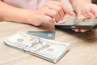 Kadın bir alışverişçi elinde cep telefonu, banknotlar ve yanında kredi kartı tutuyor. Akıllı telefon kullanarak internetten alışveriş yapmak. Tüketim ve mali tasarruflar