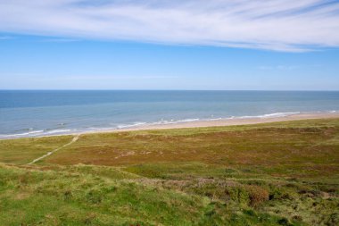 Kuzey Denizi 'nin Hilly Sahili. Güneş, mavi gökyüzü, bulutlar, dalgalar ve çimenler. Kuzey Denizi 'nin güzel manzarası. Danimarka Kıyı Manzarası