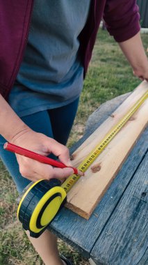 DIY. Tahta kalas ölçen bir kadın. Genç bir kadın açık havada ahşap bir kalas ölçüyor. Ev Geliştirme