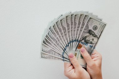 Kadın eli bize dolarları tutuyor. Kadın elleri beyaz arka planda para hayranı olduğunu gösteriyor..
