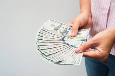 Kadın eli bize dolarları tutuyor. Kadın elleri beyaz arka planda para hayranı olduğunu gösteriyor..