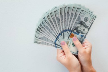 Kadın eli bize dolarları tutuyor. Kadın elleri beyaz arka planda para hayranı olduğunu gösteriyor..