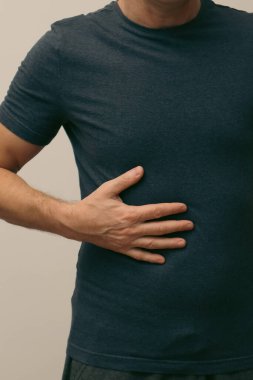 Acı çeken bir adam, ağrıyan karnını tutup sağ tarafını ovalıyor. Mide sorunları olan genç bir adam. Genç adamın tıbbi sorunları var.