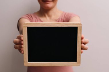 Boş tahtayı tutuyorum. Kadın elleri kara tahtayı tutuyor. Boş siyah tahta tutan bir kadının kesilmiş görüntüsü.