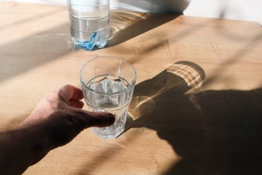 İçme suyu şişesi bardağa dökülüyor. Plastik şişeden bardağa su dökmek. Güneş gölgeleri.
