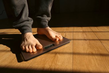 Erkek tartıda ağırlığını kontrol ediyor. Banyo üstüne ağırlık kontrolü için ayaklar. Evde ağırlık tartısı üzerinde duran bir adam. Güneş gölgeleri.