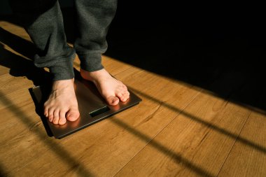 Adam, yerdeki pulları kullanarak onun ağırlığını ölçüyor. İnsan ve kilo kaybı. Güneşli bir sabahta Gölge.