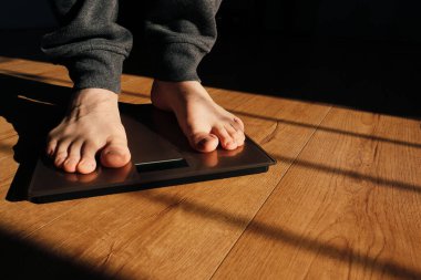 Erkek tartıda ağırlığını kontrol ediyor. Banyo üstüne ağırlık kontrolü için ayaklar. Evde ağırlık tartısı üzerinde duran bir adam. Güneş gölgeleri.