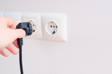 Elektrik kablosunu sokete takan ya da çıkaran adam. Duvarda elektrik kabloları ve güç bantları var.