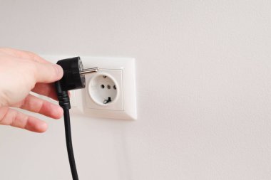 Elektrik kablosunu sokete takan ya da çıkaran adam. Duvarda elektrik kabloları ve güç bantları var.