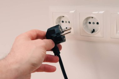 Elektrik kablosunu sokete takan ya da çıkaran adam. Duvarda elektrik kabloları ve güç bantları var.