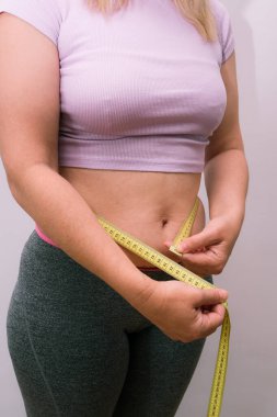 Kilo kaybı diyeti ya da yağ aldırma sonucu tanınmayan bir bayan. Şişman göbeğini ölçen şişman bir kadın. Güzellik, şekil, sağlıklı ve sağlık hizmetleri kadın konsepti.