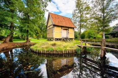 Tipik bir ahşap kulübe, yarım ahşap yapı ve çamurla çevrili hendek ve cennet bahçesi, çiçek açan çiçekler ve Bad Zwischenahn (Almanya) kaplıca parkındaki ahşap köprü.)