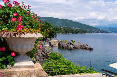 Hırvatistan 'ın Lovran kentinde ön planda büyük bir çiçek kasesi bulunan güzel kıyı şeridi.