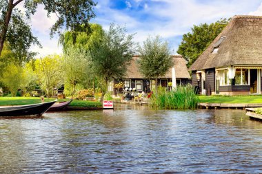 Saz çatılı kulübeleri ve tekneleri olan sakin bir nehir kenarı köyü.