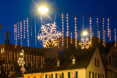 Mavi saatte şehirde kar taneleri ve hafif tellerle aydınlatılmış Noel ışıklandırması