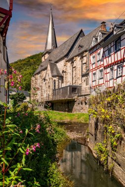 Monreal 'deki Trinity Kilisesi-Dreifaltigkeitskirche. Güneşli bir yaz gününde yarım ahşap evler ve dereyle.