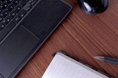 Siyah bir dizüstü bilgisayar ahşap bir masada defter ve kalemle fotoğraflanır.