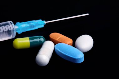 Plastik şırınga ve ilaçların siyah arka plan, kenar görüş, tıp ve sağlık hizmetleri kavramında fotoğraflandığı tabletler
