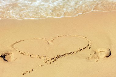 Deniz kumlarında akan beyaz deniz köpüğüyle boyanmış bir kalp, kalbin sembolü, aşk kavramı.