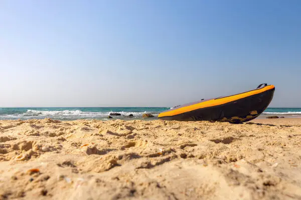 Kırmızı kauçuk bir tekne kumlu bir plajda yatıyor. Arkasında deniz ve açık mavi bir gökyüzü var. Denizde verimli bir tatil kavramı, sağlıklı bir yaşam tarzıyla birlikte sunuluyor.
