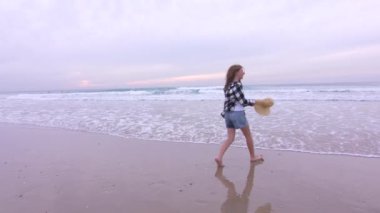 Gün batımında deniz kıyısında dans eden ve dalgalarla dalga geçen tatlı bir genç kız. Yüksek kalite 4k görüntü