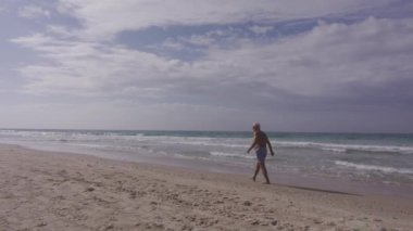 Mayo giyen son sınıf öğrencisi okyanus boyunca sahilde yürüyüş yapıyor. Yüksek kalite 4k görüntü