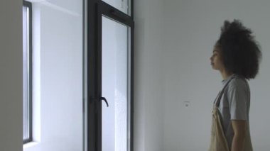 Genç bir kadın yaklaşır ve parlak yeni bir odada cam bir balkon kapısını açar. Yüksek kaliteli 4K yaşam tarzı görüntüleri.