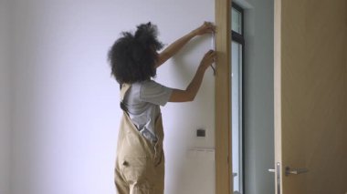 Genç bir kadın, parlak ve yeni yenilenmiş bir odada bir mezura kullanarak kapı aralığının kesin ölçümlerini alıyor. 4k görüntü