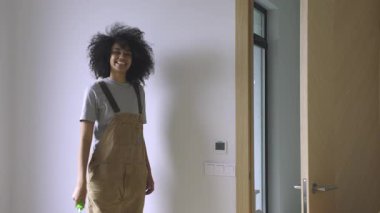 Girişte duran genç bir kadın, elinde güneşli bir alanda boya silindiri sallıyor, 4K 'lık kaliteli bir görüntü..