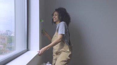 Genç bir bayan güneşli bir duvara boya sürmek için bir silindir kullanıyor. Yüksek kalite 4K video.