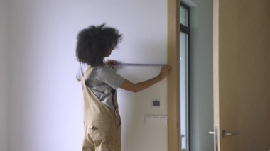 Ölçüm bandı kullanan bir kadın, güneşli, yenilenmiş bir iç mekanda bir kapının mimari boyutlarını kontrol eder. 4K.