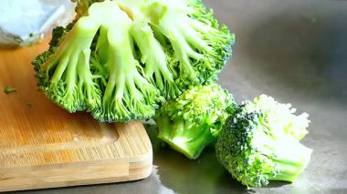 Mutfaktaki bir tahtada brokoli kesiyor..