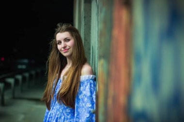 Geceleri mavi elbiseli genç bir kadın, şehir duvarının yanında poz veriyor.