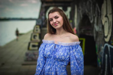 Geceleri mavi elbiseli genç bir kadın, şehir duvarının yanında poz veriyor.