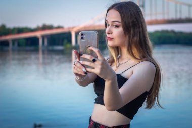Gün batımında nehirden selfie çeken genç bir kadın.